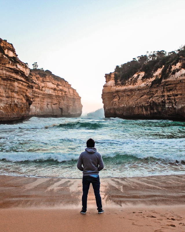 A young man looks at the ocean seen through a narrow gap in cliffs